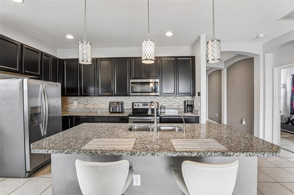 A kitchen with dark cabinets, granite countertops, a central island, and three hanging pendant lights — 365 JYOTI DRIVE, DAVENPORT, FL