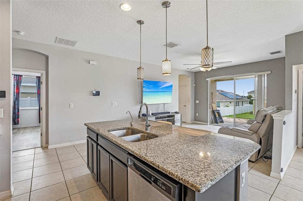 A kitchen island with granite countertops overlooks a living area with a television and patio — 365 JYOTI DRIVE, DAVENPORT, FL