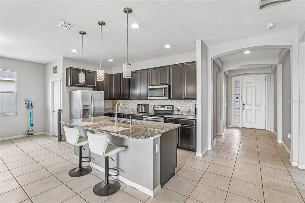 A kitchen features dark wood cabinets, granite countertops, a center island, and tile flooring — 365 JYOTI DRIVE, DAVENPORT, FL