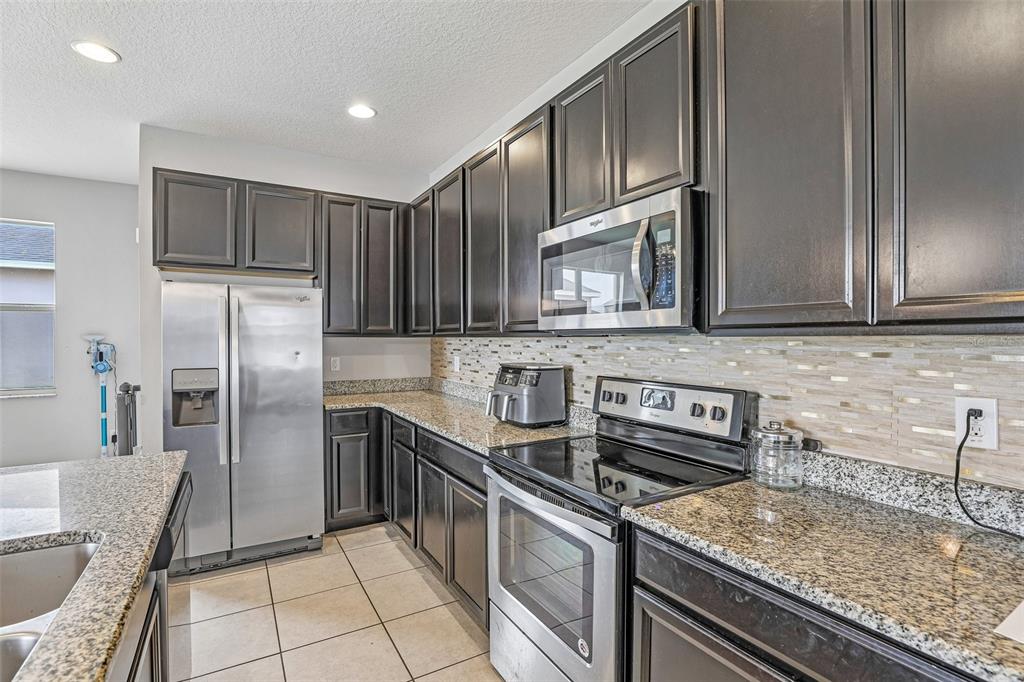 A kitchen features dark wood cabinets, granite countertops, stainless steel appliances, and a tiled floor — 365 JYOTI DRIVE, DAVENPORT, FL