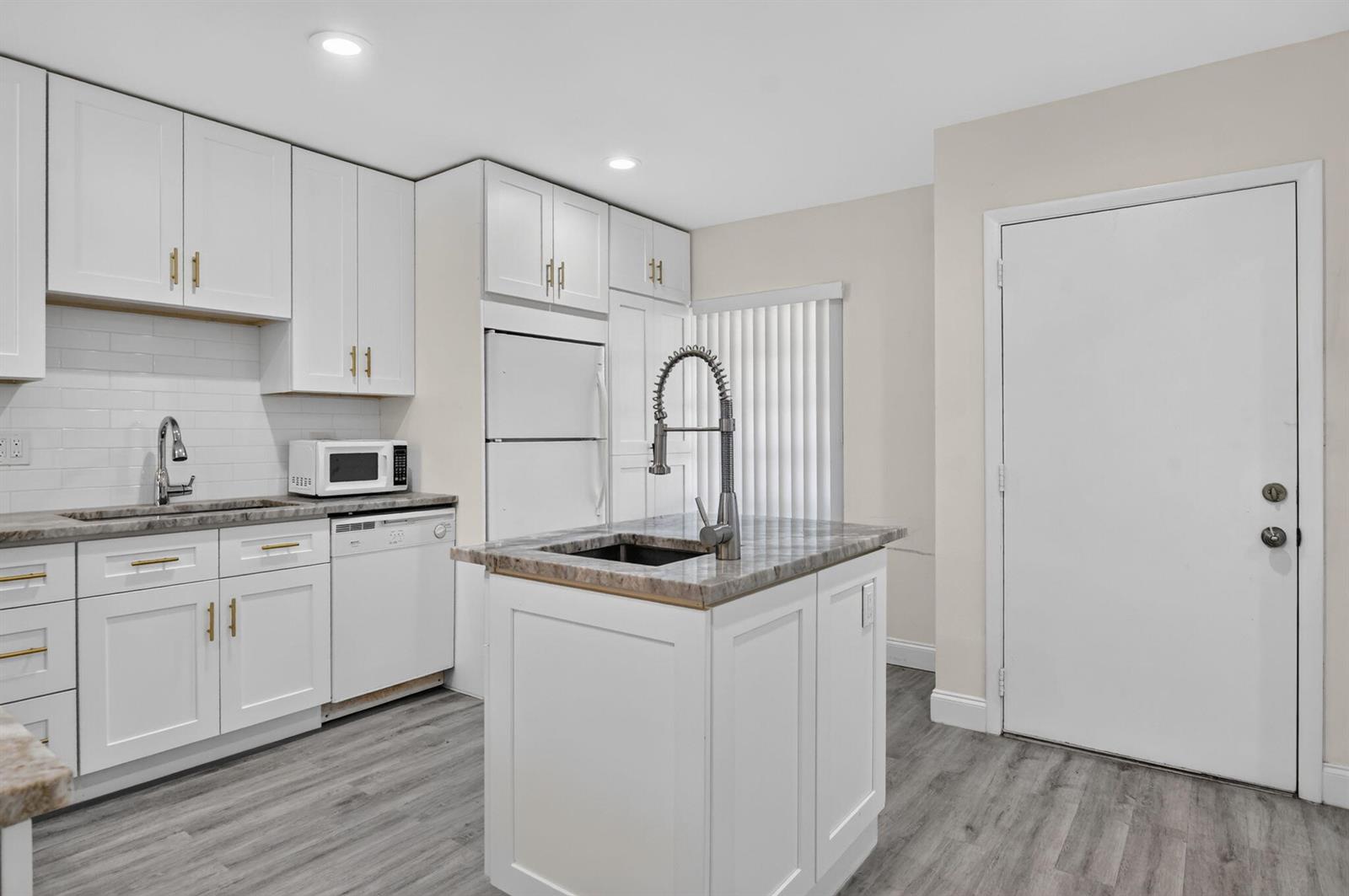 A kitchen features white cabinets, a central island with a sink, and gray wood flooring — 20846 Vinesta Circle, Boca Raton FL 33433, BOCA RATON, FL