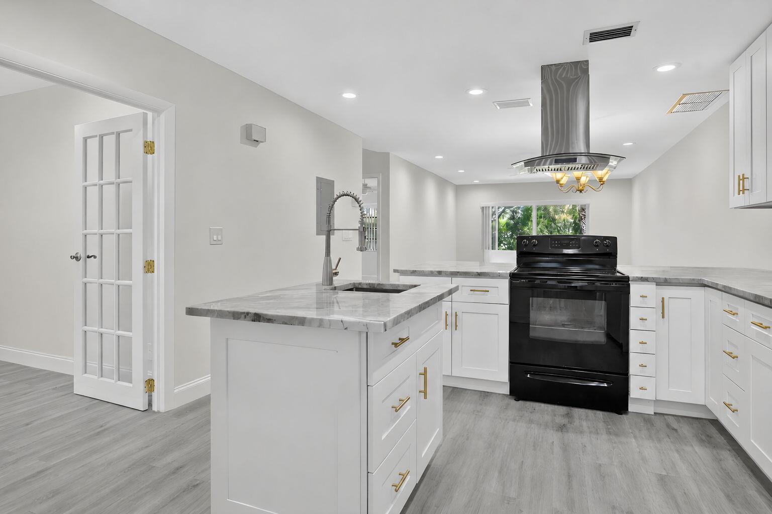 A kitchen features white cabinets, a marble-topped island, a black stove, and gray flooring — 20846 Vinesta Circle, Boca Raton FL 33433, BOCA RATON, FL