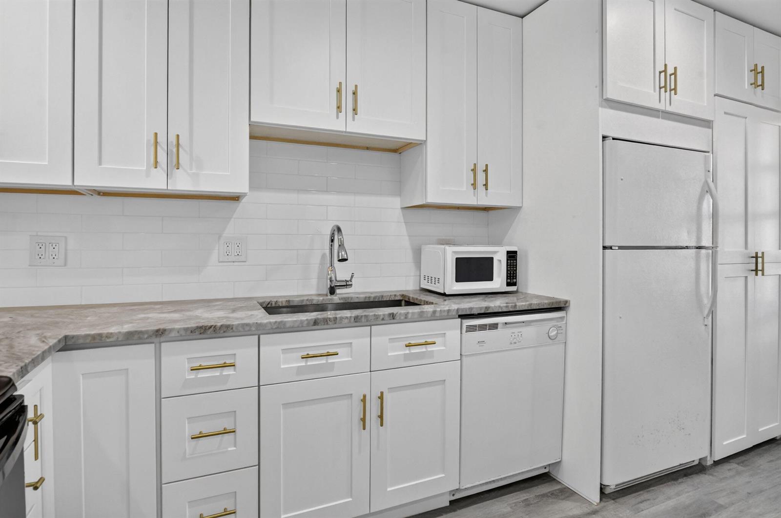 A kitchen features white cabinets, gold hardware, a marble-look countertop, and a white dishwasher — 20846 Vinesta Circle, Boca Raton FL 33433, BOCA RATON, FL