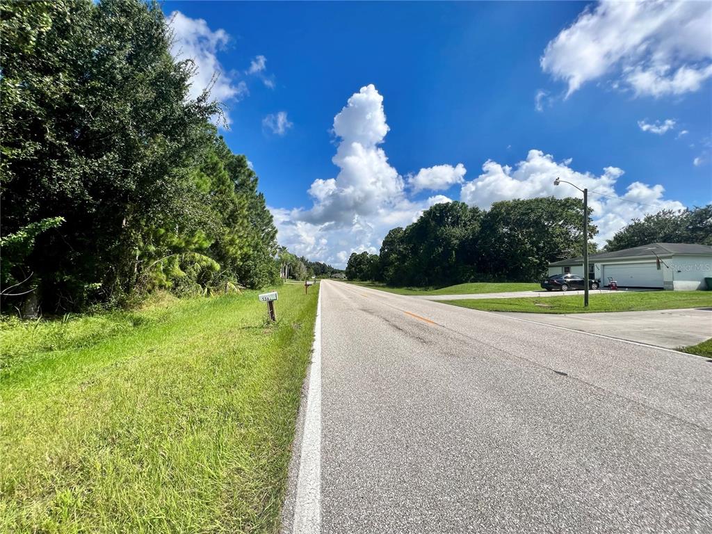 A paved road stretches into the distance past a grassy shoulder and a residential house — 5552 GILLOT BOULEVARD, PORT CHARLOTTE, FL