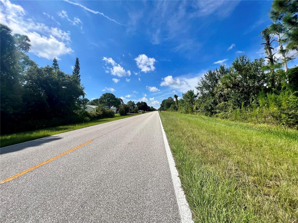 A paved two-lane road stretches into the distance between grassy shoulders and dense trees — 5552 GILLOT BOULEVARD, PORT CHARLOTTE, FL
