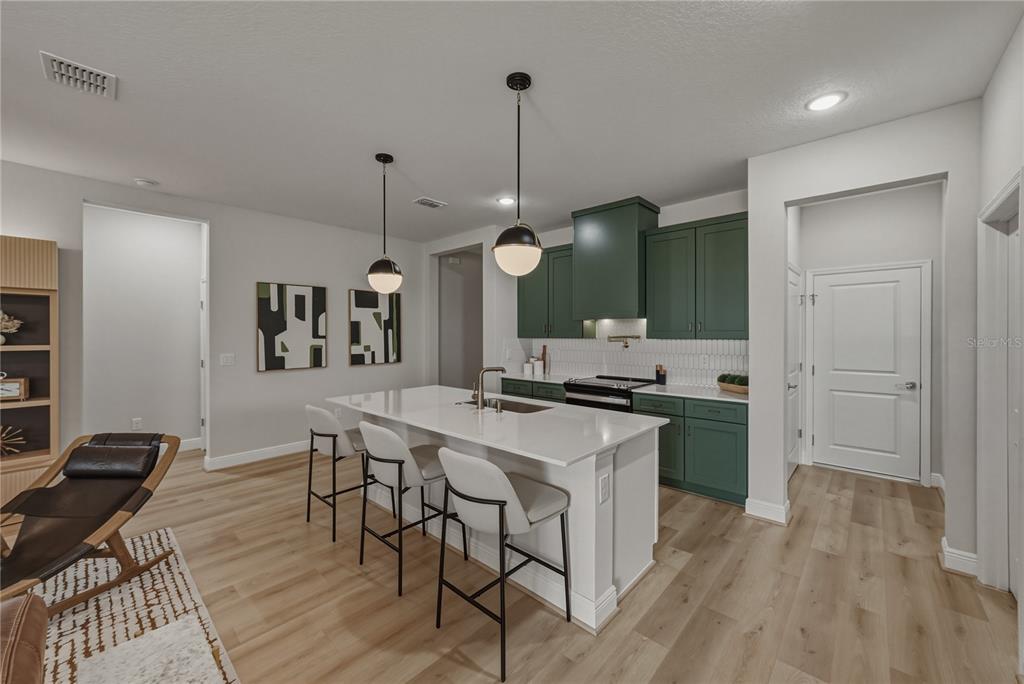 A kitchen features a white island with bar stools, green cabinets, and light wood flooring — 10368 FIELDSTONE MYRTLE WAY, SAN ANTONIO, FL