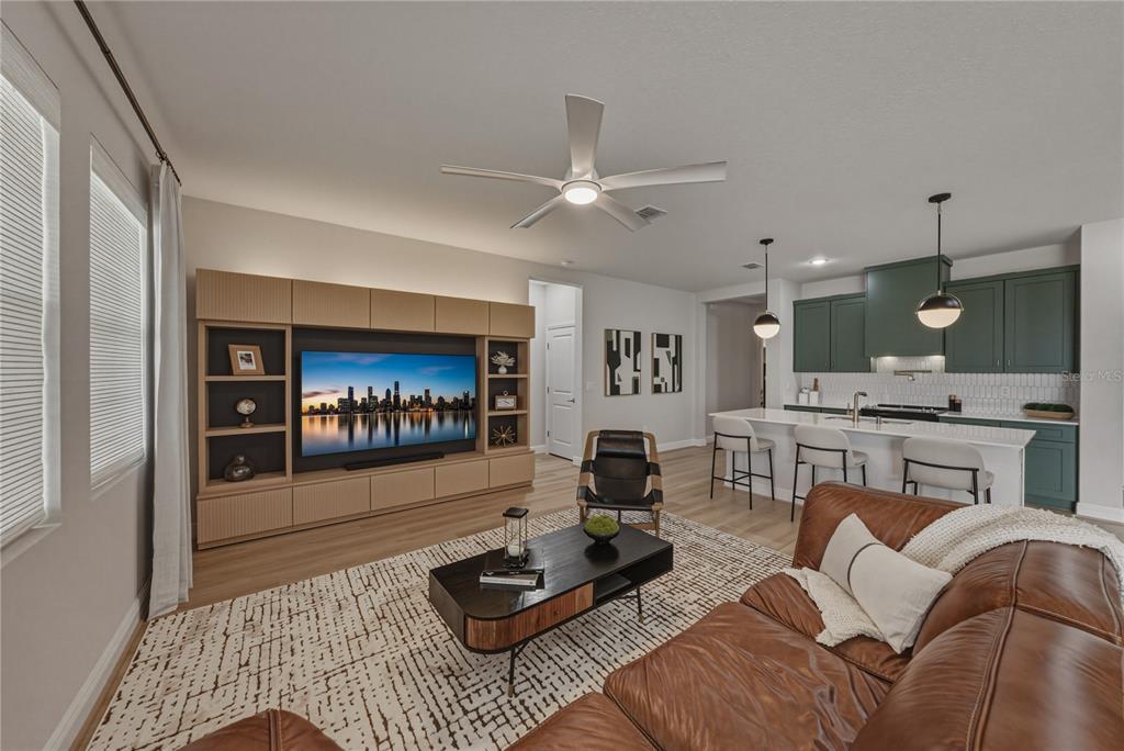 A living room with a large media console, leather sofa, and an open kitchen island — 10368 FIELDSTONE MYRTLE WAY, SAN ANTONIO, FL