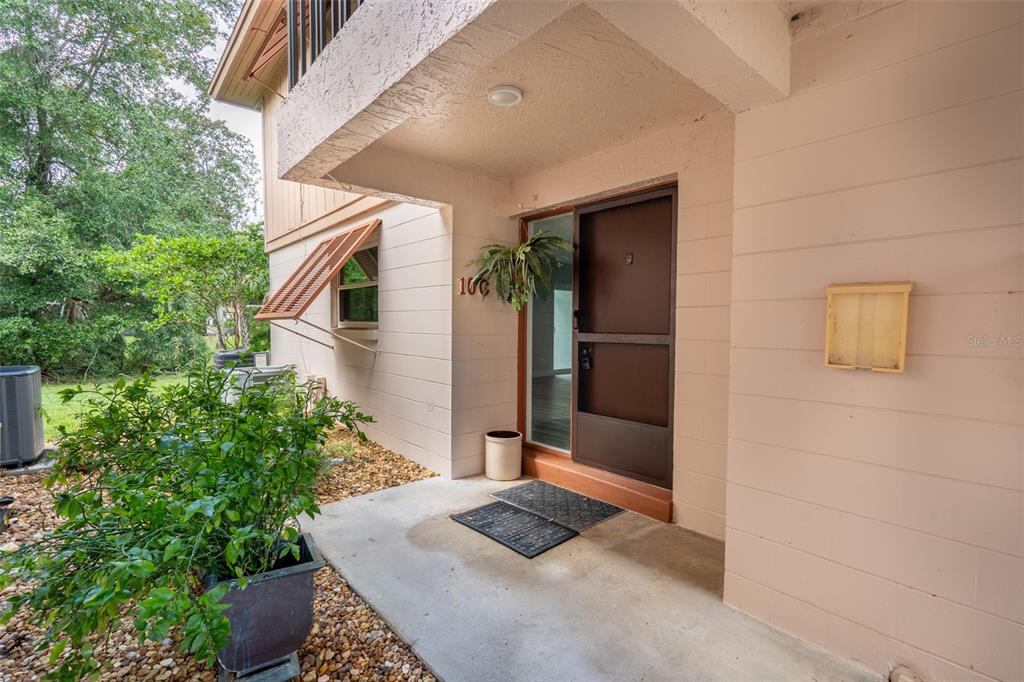 The exterior entrance of a home features a brown door, a porch, and a plant — 100 SWEETGUM WOODS COURT UNIT 10C, DELTONA, FL