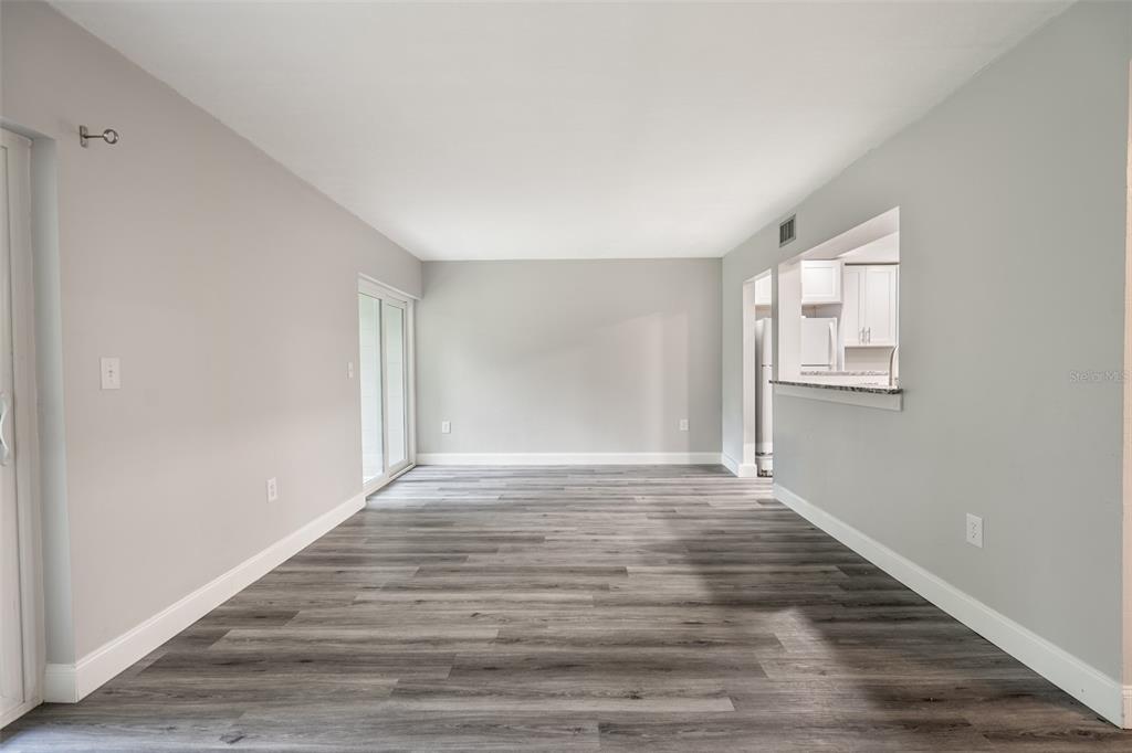 An empty living room features gray walls, wood-look flooring, and a pass-through to the kitchen — 100 SWEETGUM WOODS COURT UNIT 10C, DELTONA, FL