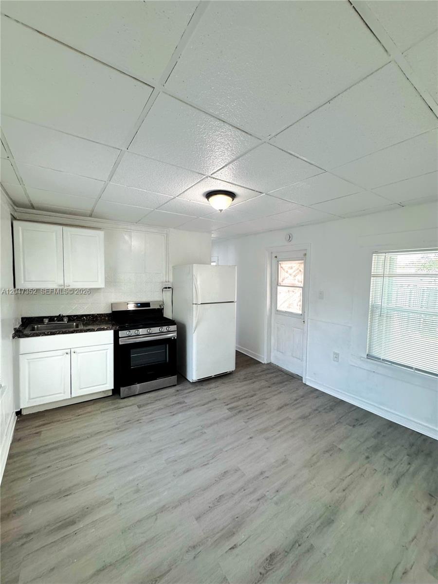A kitchen features white cabinets, a black stove, a white refrigerator, and wood-look flooring — DANIA BEACH, FL