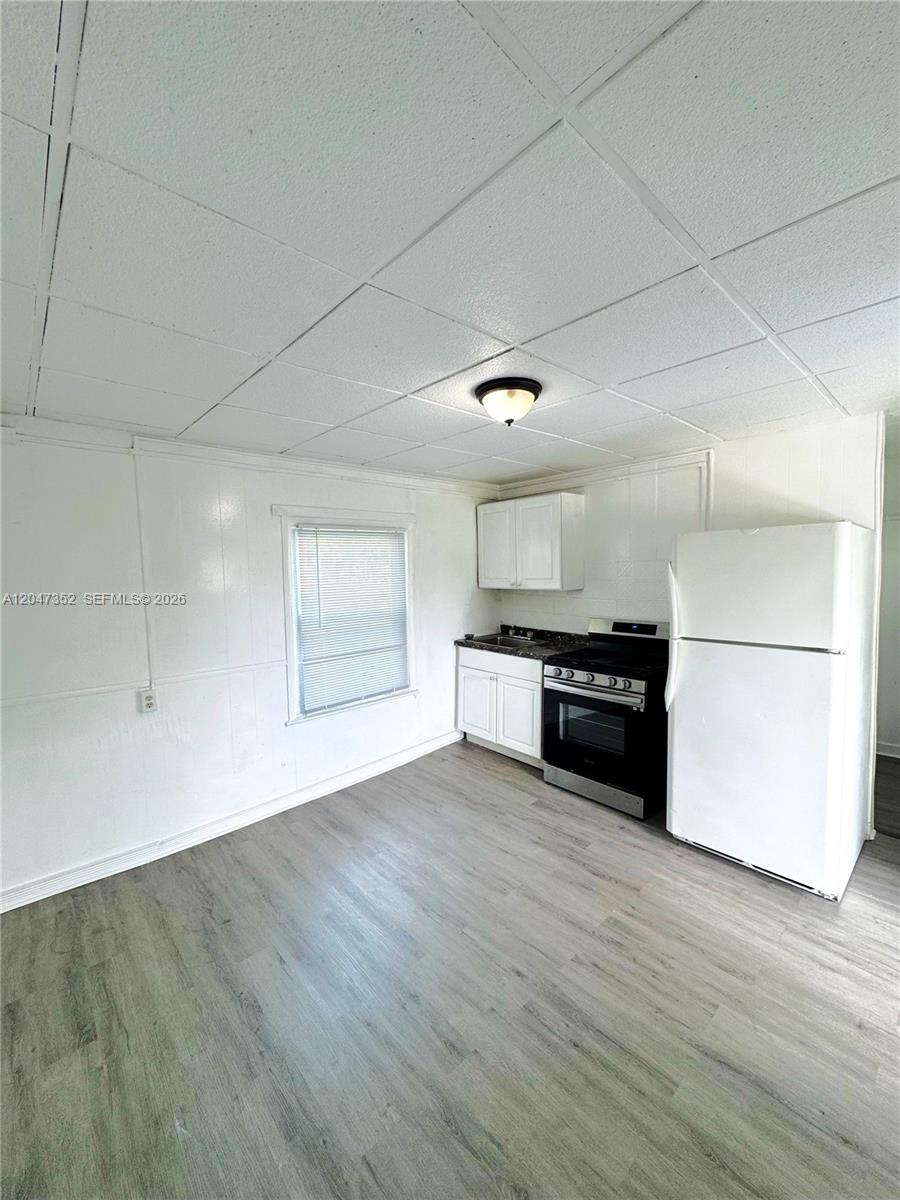 A small kitchen features white cabinets, a black stove, a white refrigerator, and wood-look flooring — DANIA BEACH, FL