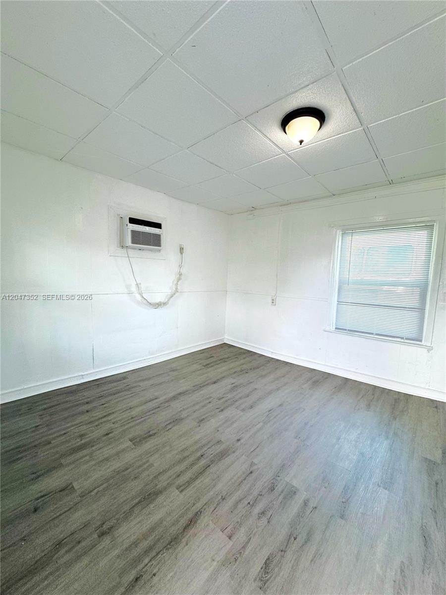 An empty room features white walls, a drop ceiling, and gray wood-look flooring — DANIA BEACH, FL