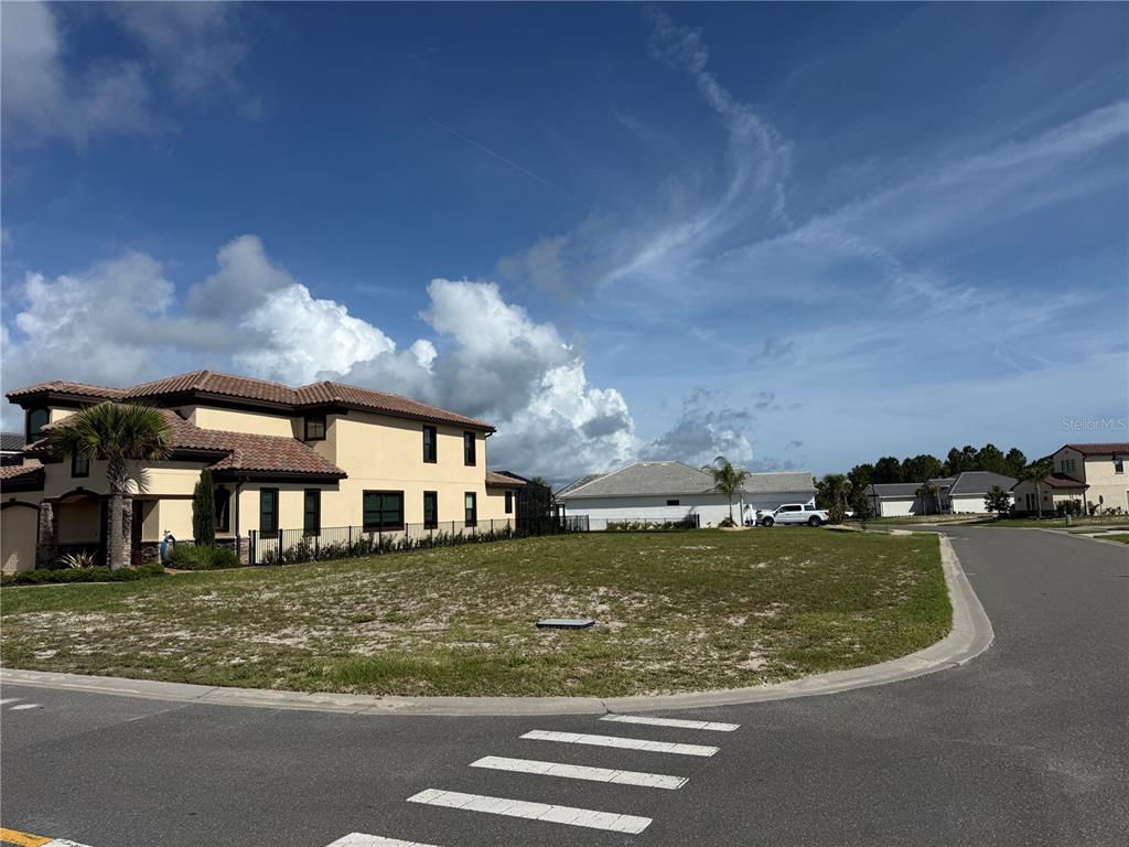 A vacant corner lot sits next to a two-story stucco house with a tile roof — 1 MENORCA WAY, PALM COAST, FL