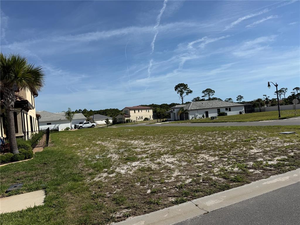 A vacant residential lot sits between existing houses under a blue sky — 1 MENORCA WAY, PALM COAST, FL