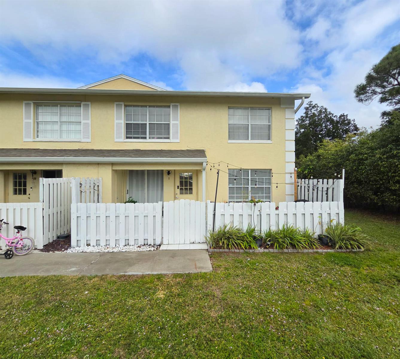 A two-story yellow townhouse features a white picket fence enclosing a small front patio — 222 Foxtail Drive # I, FL 33415, FL