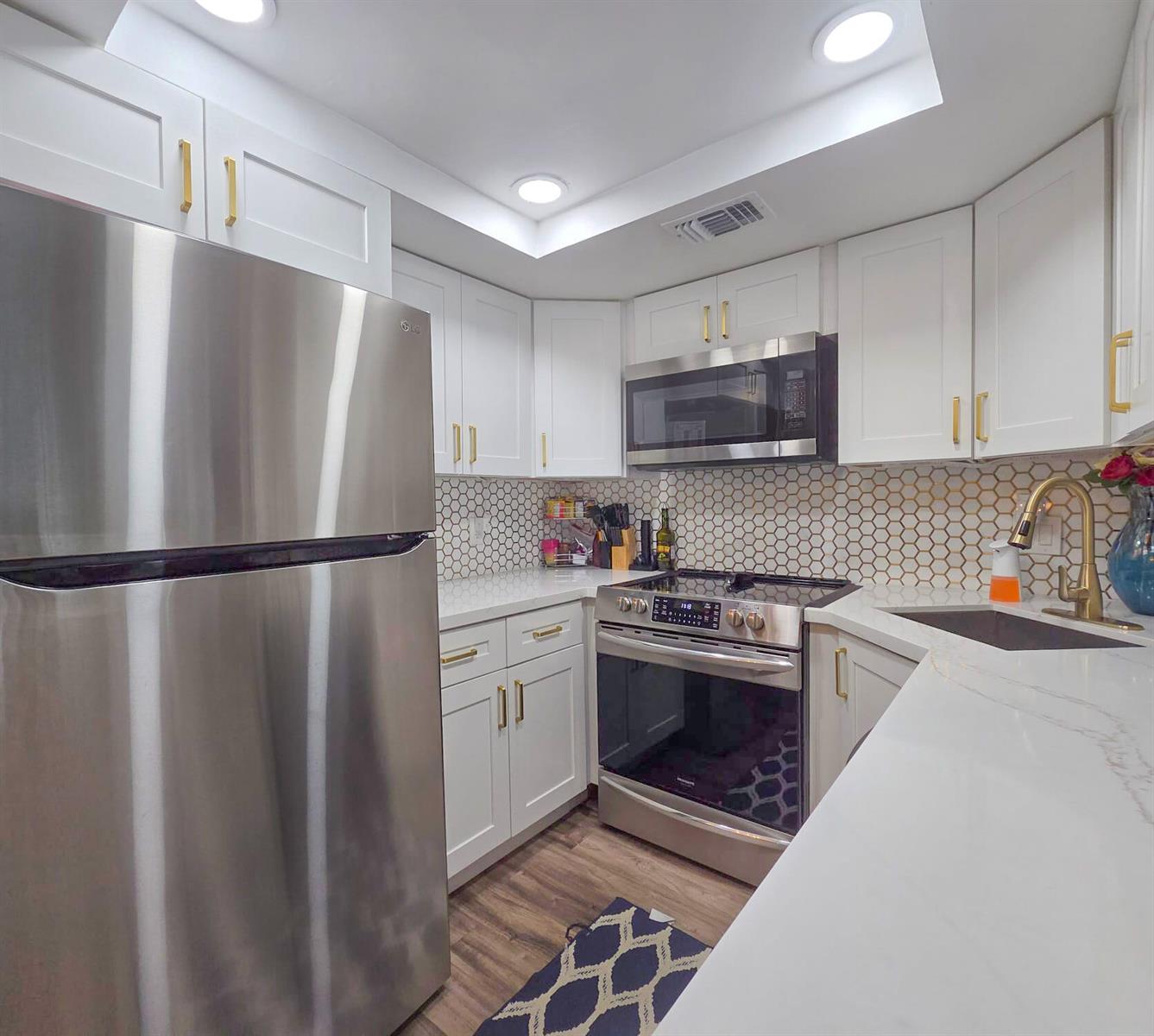 A kitchen features white cabinets, gold hardware, stainless steel appliances, and a hexagonal tile backsplash — 222 Foxtail Drive # I, FL 33415, FL