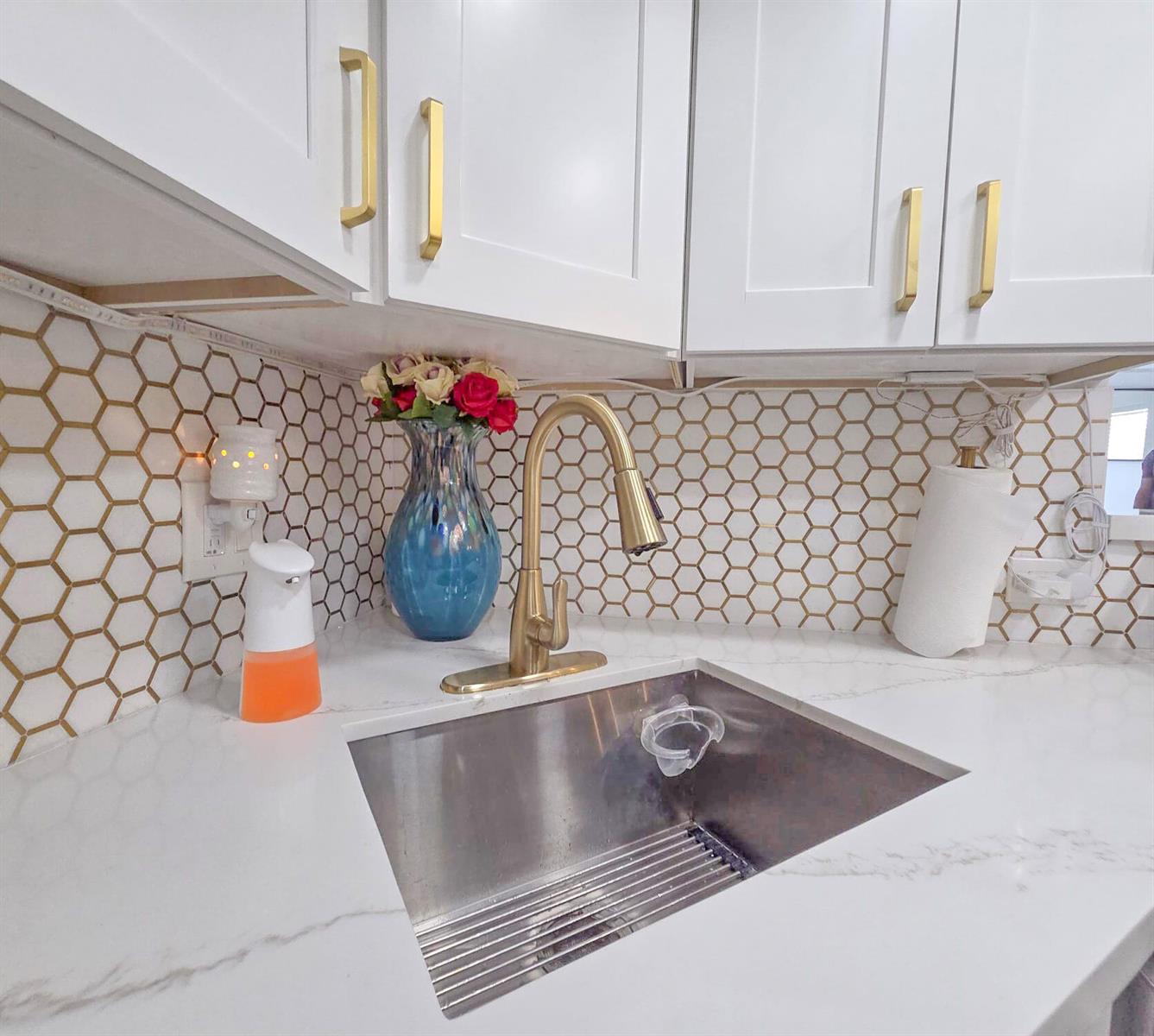 A kitchen sink area features white cabinets, gold hardware, and a gold-accented hexagonal tile backsplash — 222 Foxtail Drive # I, FL 33415, FL