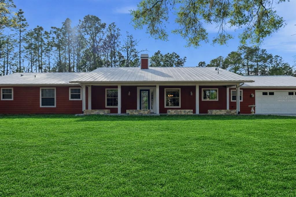 A single-story red house with a white metal roof and a large green lawn — 12092 S HYACINTH POINT, FLORAL CITY, FL