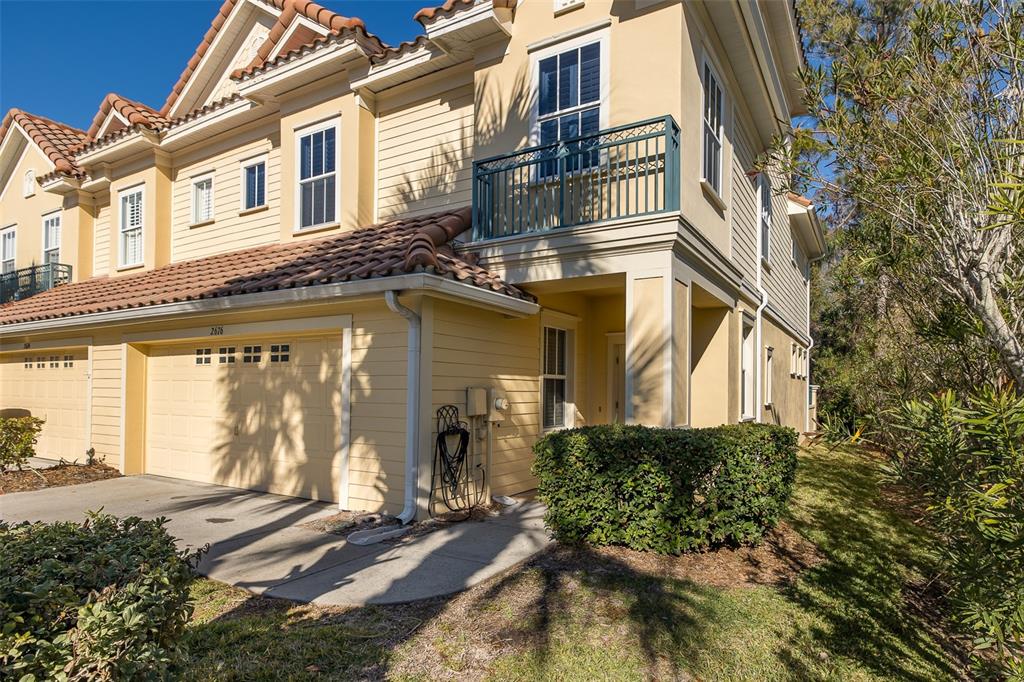 A two-story yellow townhouse with a tile roof, a garage, and a second-floor balcony — 2676 TANGLEWOOD TRAIL, PALM HARBOR, FL