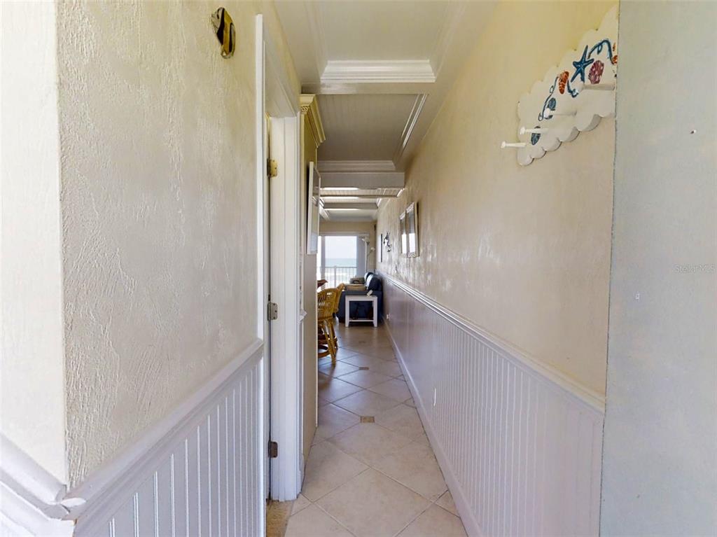 A hallway with beadboard wainscoting and tile flooring leads toward a room with ocean views — 4849 SAXON DRIVE UNIT 2030, NEW SMYRNA BEACH, FL