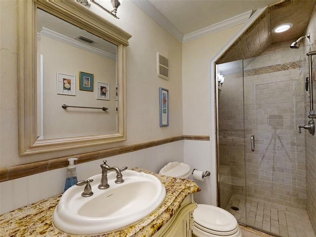 A bathroom features a granite vanity, a framed mirror, and a glass-enclosed tiled shower — 4849 SAXON DRIVE UNIT 2030, NEW SMYRNA BEACH, FL
