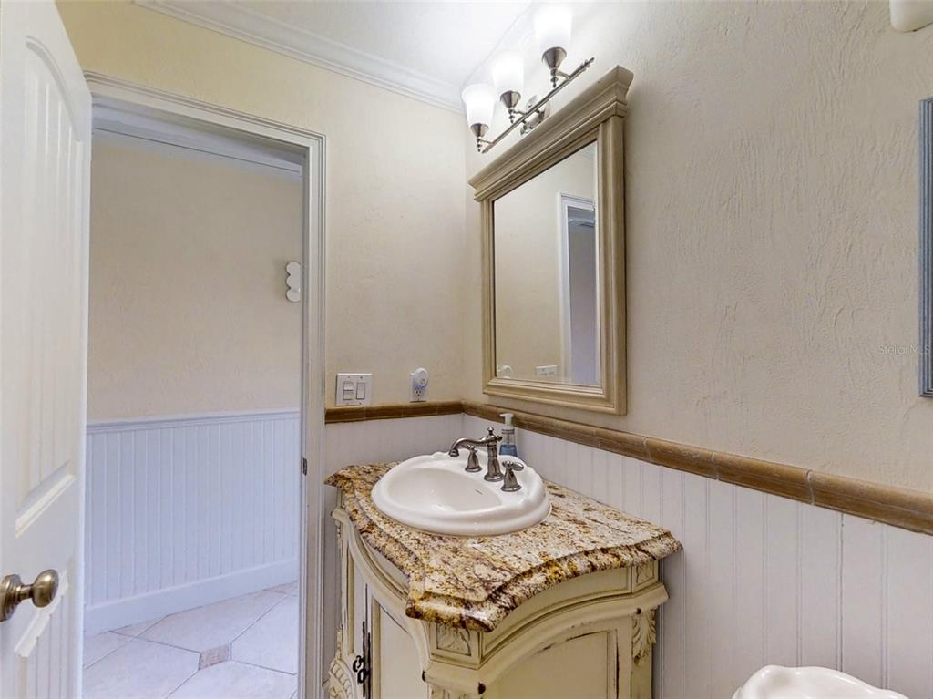 A bathroom features a granite-topped vanity, a framed mirror, and white wainscoting on the walls — 4849 SAXON DRIVE UNIT 2030, NEW SMYRNA BEACH, FL