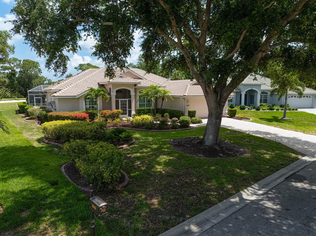 A single-story house with a tile roof, large tree, and landscaped yard in a neighborhood — 2025 WHITE FEATHER LANE, NOKOMIS, FL