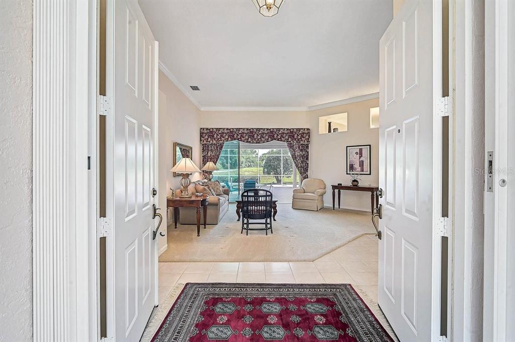 A view through double doors into a living room with carpeted floors and a large window — 2025 WHITE FEATHER LANE, NOKOMIS, FL