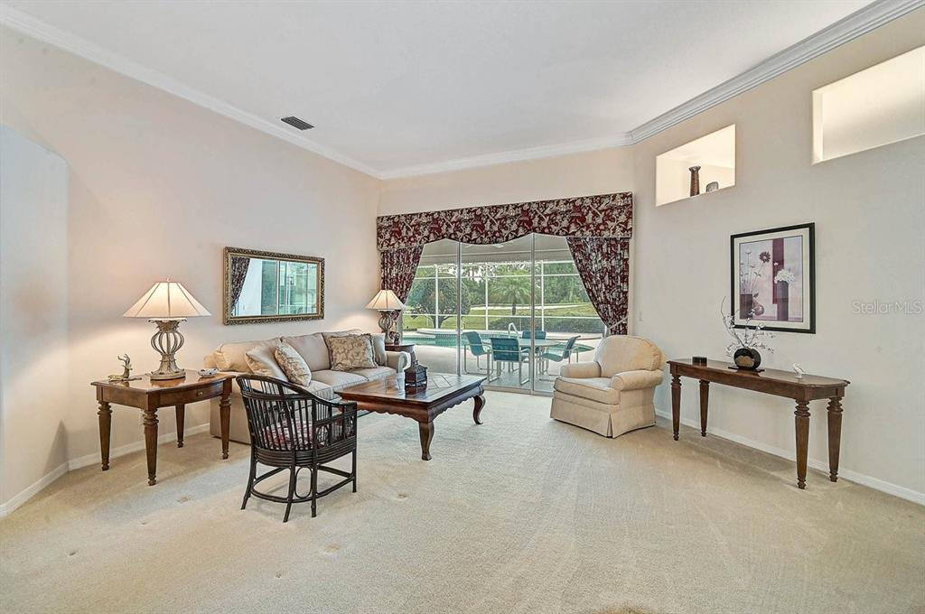 A living room features beige carpet, a sofa, armchairs, and sliding doors leading to a pool — 2025 WHITE FEATHER LANE, NOKOMIS, FL