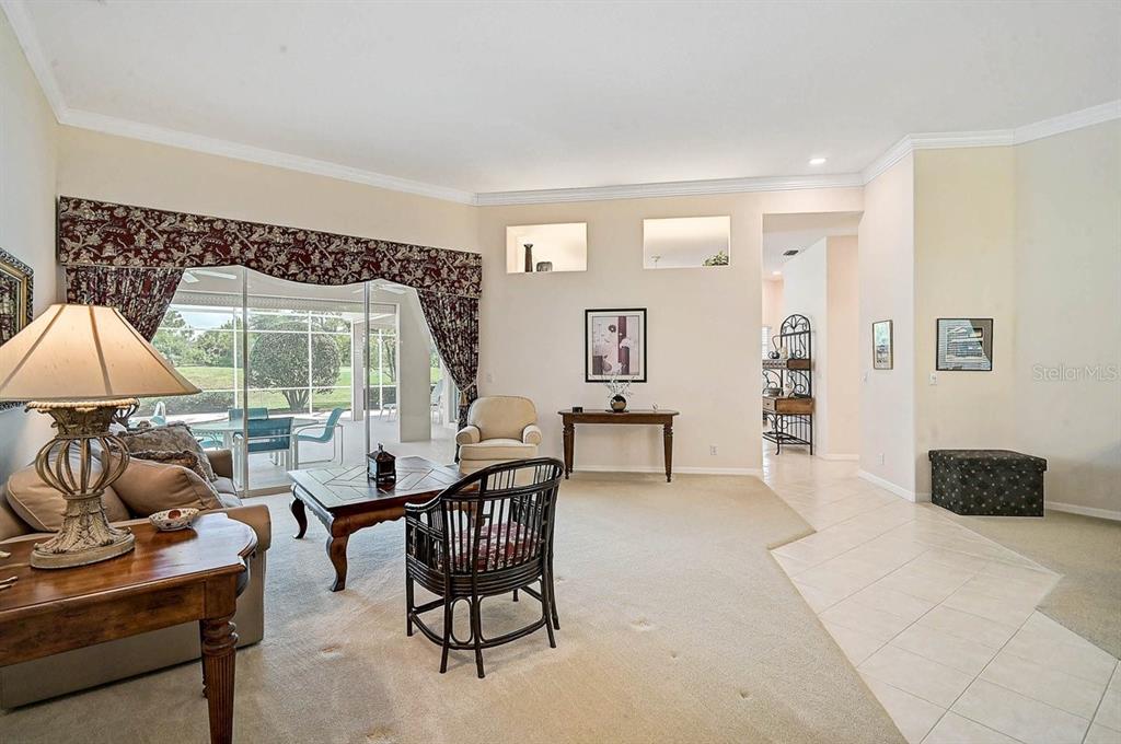 A living room with beige carpet, a sliding glass door, and a tiled entryway — 2025 WHITE FEATHER LANE, NOKOMIS, FL