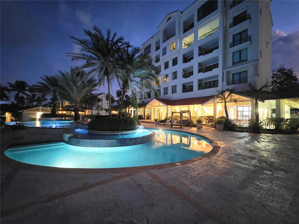 A multi-story building overlooks a swimming pool with fountains at dusk — 9000 RIO MAR  BOULEVARD UNIT 443, RIO GRANDE, PR