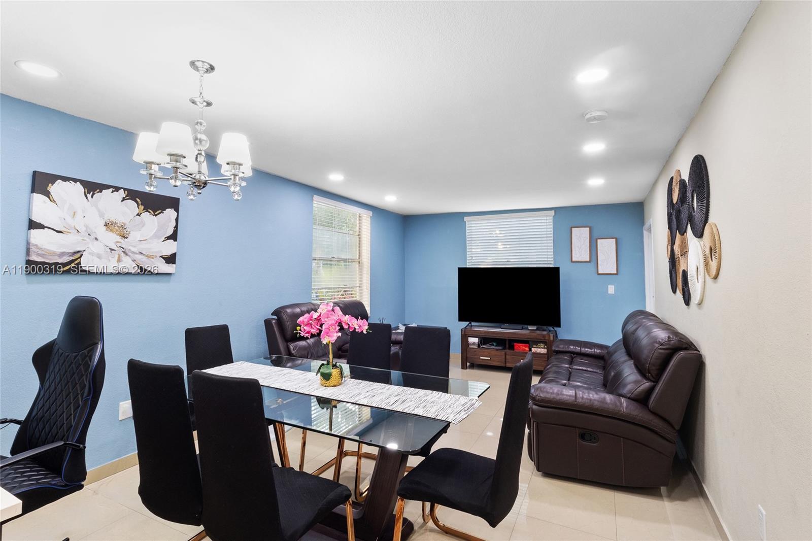 A dining area with a glass table and black chairs sits adjacent to a living space — 5665 W 20th Ave # 212, Hialeah FL 33012, HIALEAH, FL