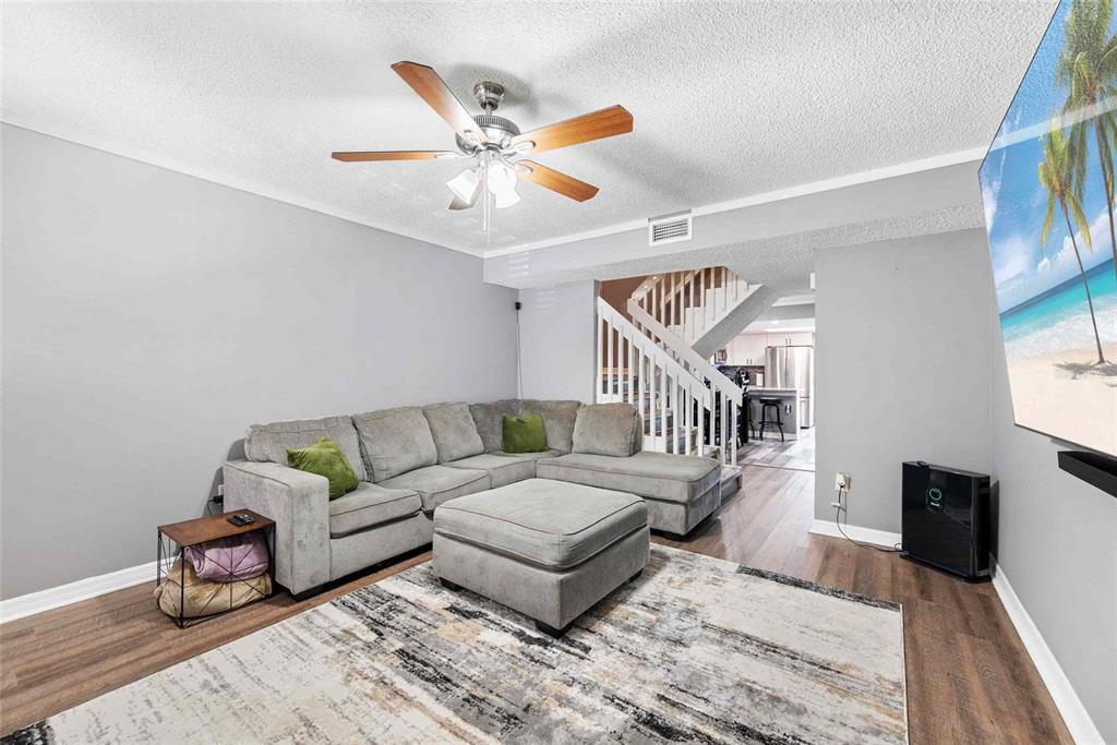 A living room features a gray sectional sofa, a matching ottoman, and wood-look flooring — 3350 FOX HUNT DRIVE, PALM HARBOR, FL
