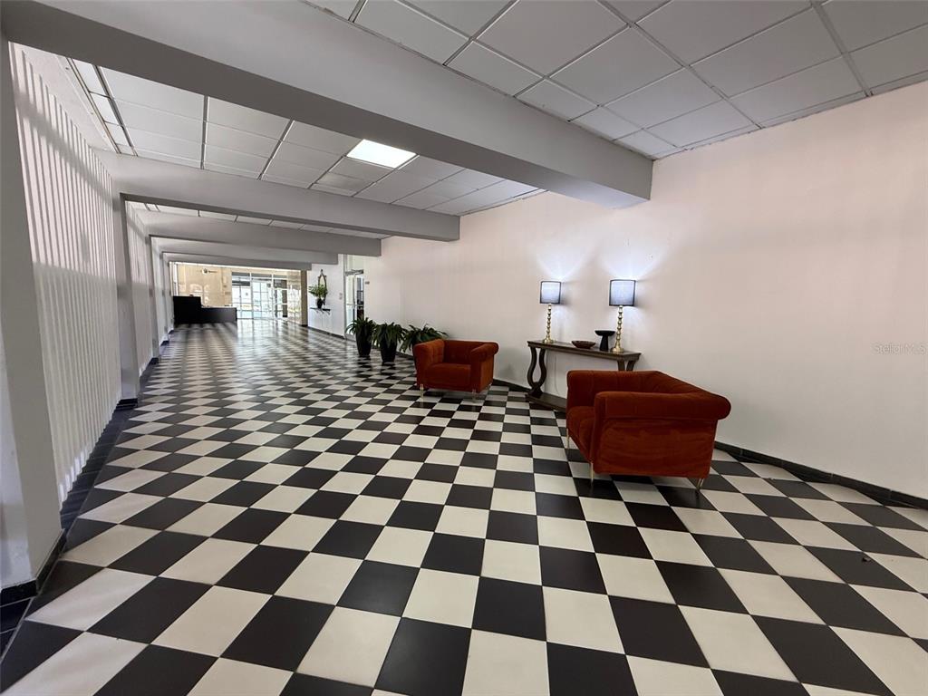 A long hallway features a black and white checkered floor, two orange chairs, and lamps — MIRAMAR TOWERS 721 HERNANDEZ ST. UNIT 12 D, SAN JUAN, PR