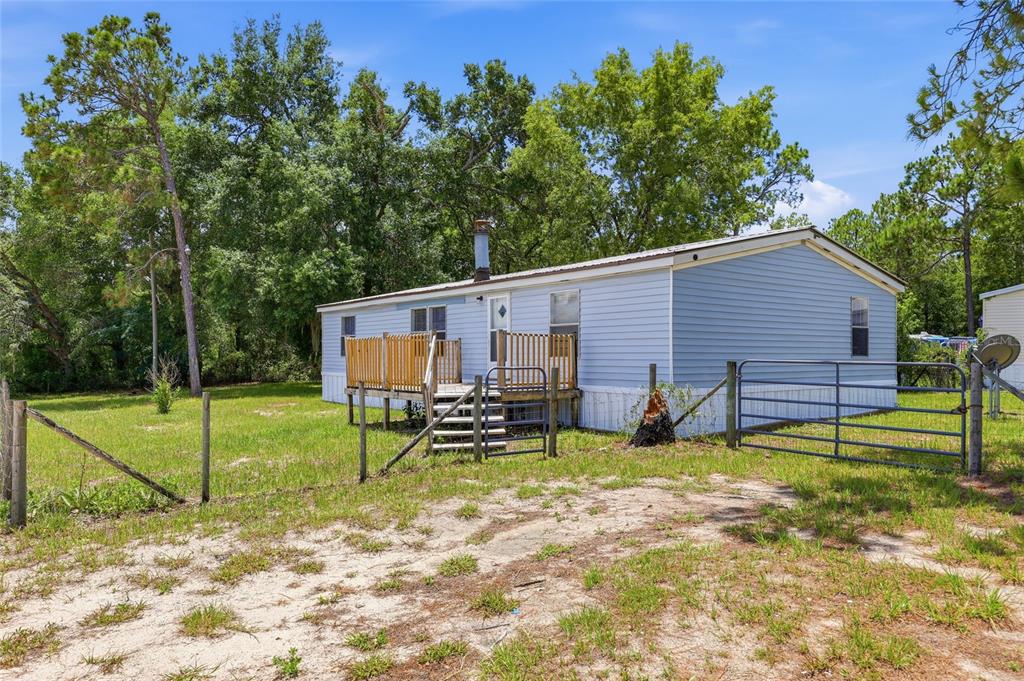 A light blue mobile home with a wooden deck stands on a grassy, fenced lot — 350 ISHIE AVENUE, BRONSON, FL