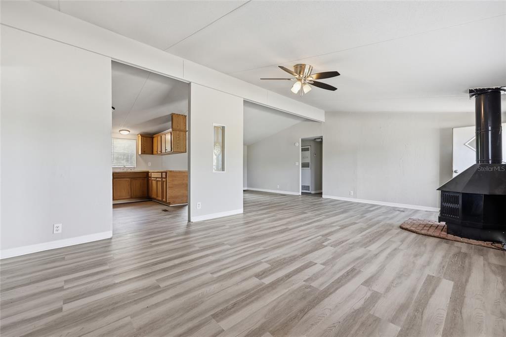 A living room with light wood-look flooring and a black fireplace leads to a kitchen — 350 ISHIE AVENUE, BRONSON, FL