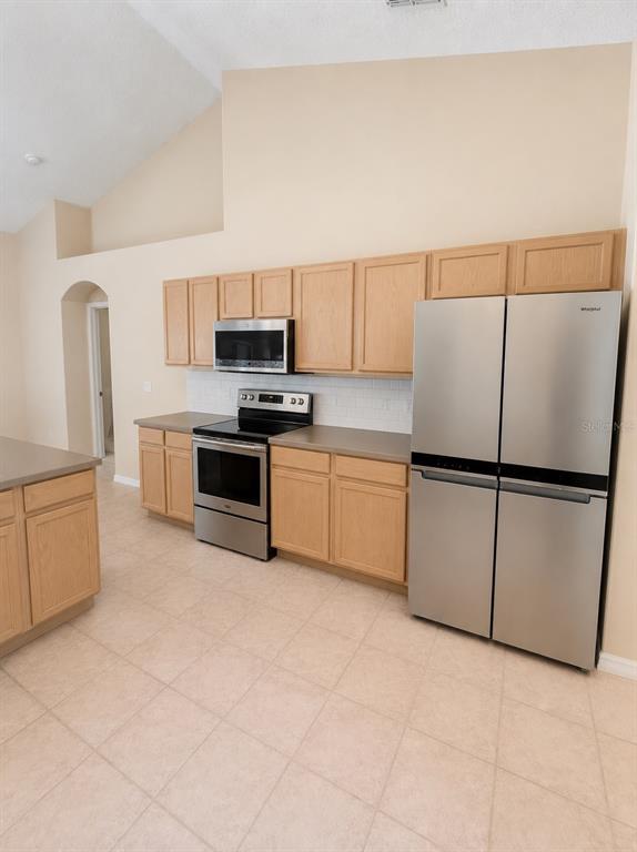 A kitchen features light wood cabinets, stainless steel appliances, and tile flooring — 15849 MERCOTT COURT, CLERMONT, FL