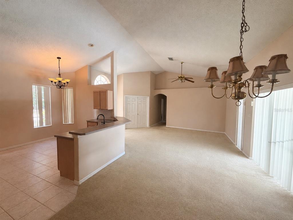 A living room with beige carpet, a kitchen island, and a dining area with tile flooring — 15849 MERCOTT COURT, CLERMONT, FL
