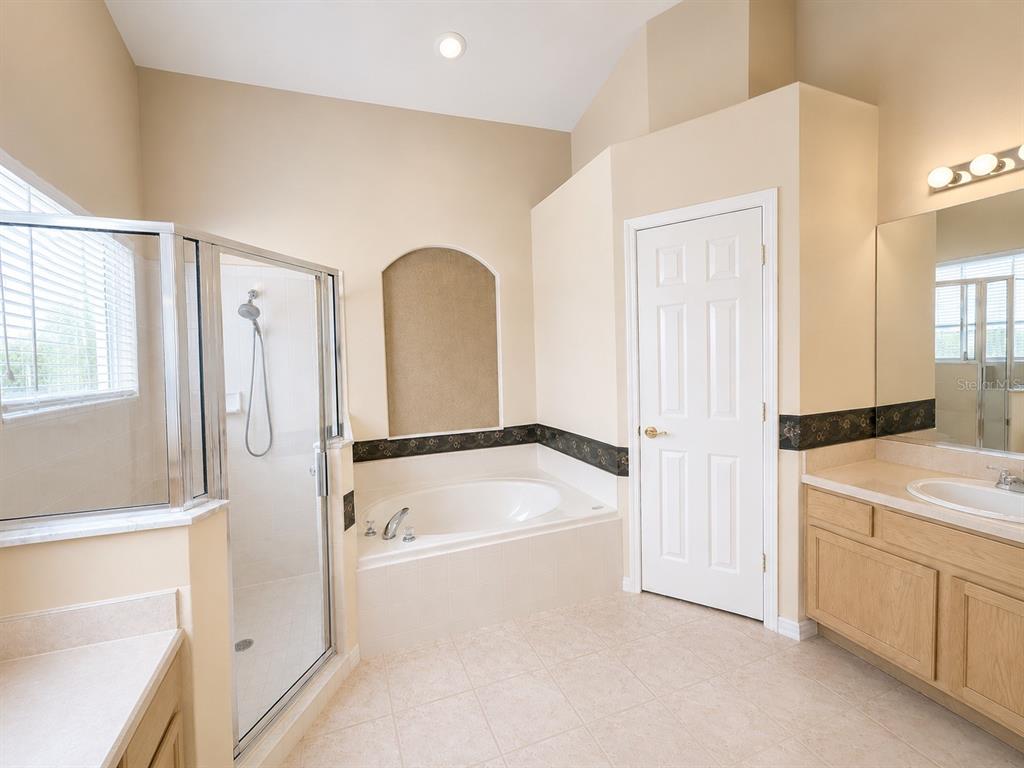 A bathroom features a corner shower, a soaking tub with an arched niche, and vanity cabinets — 15849 MERCOTT COURT, CLERMONT, FL