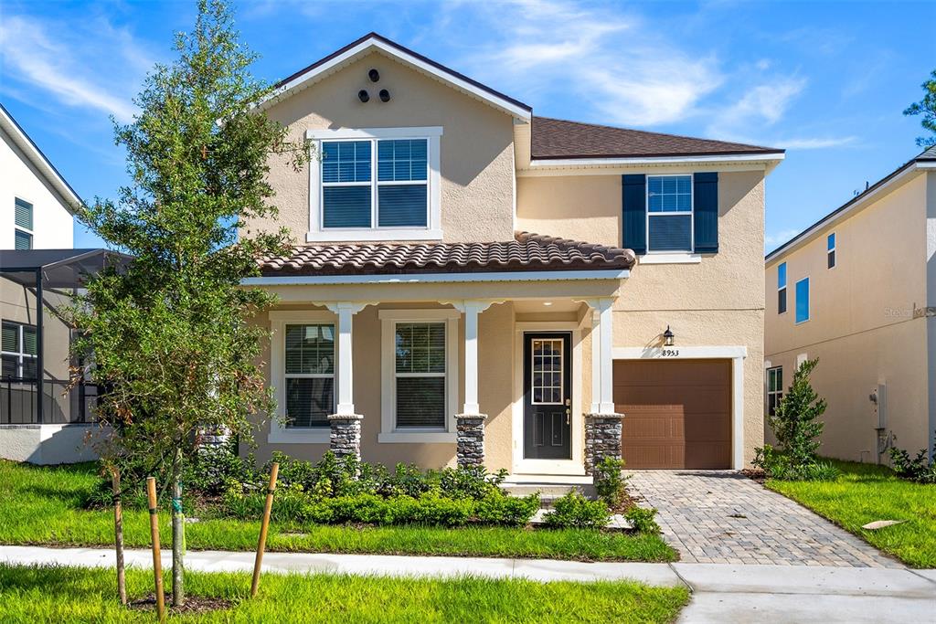 A two-story suburban house with a tan stucco exterior, brown garage door, and front porch — 8953 COCONUT BREEZE DRIVE, KISSIMMEE, FL