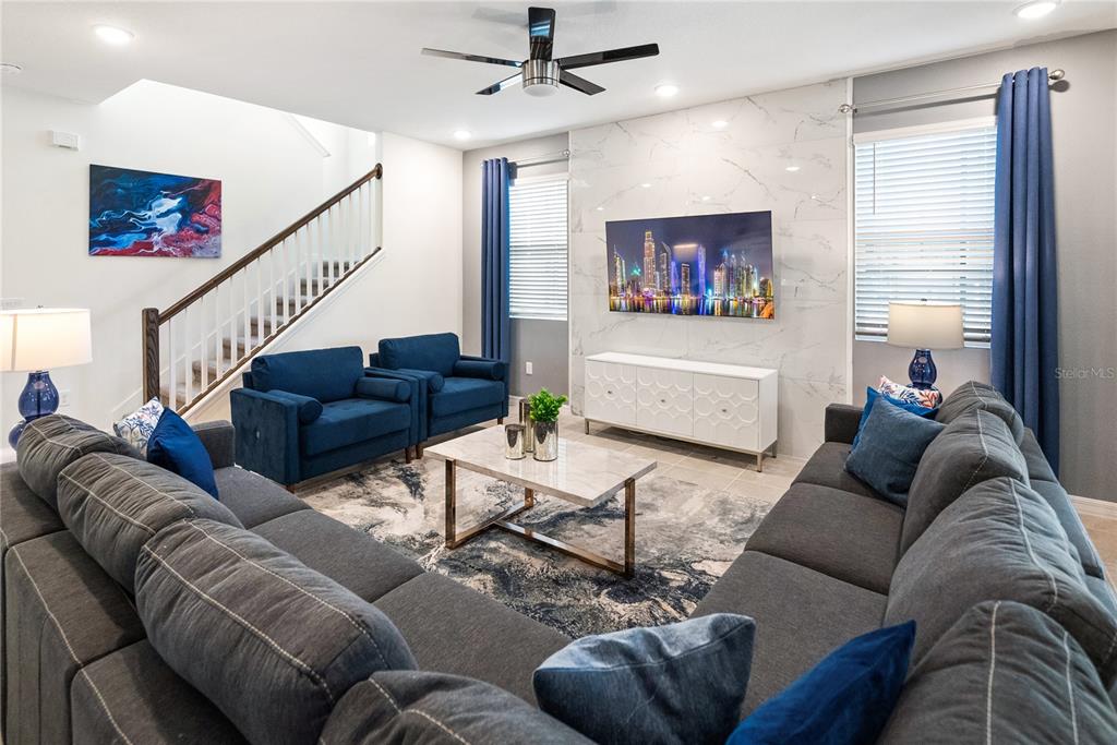 A living room features a marble accent wall, a large sectional, and a staircase — 8953 COCONUT BREEZE DRIVE, KISSIMMEE, FL
