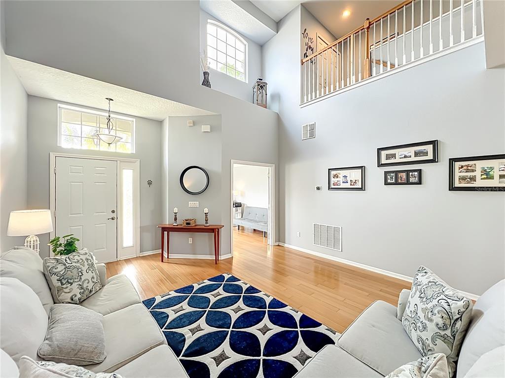 A two-story living room features light gray walls, hardwood floors, and a blue patterned rug — 949 PICKFAIR TERRACE, LAKE MARY, FL