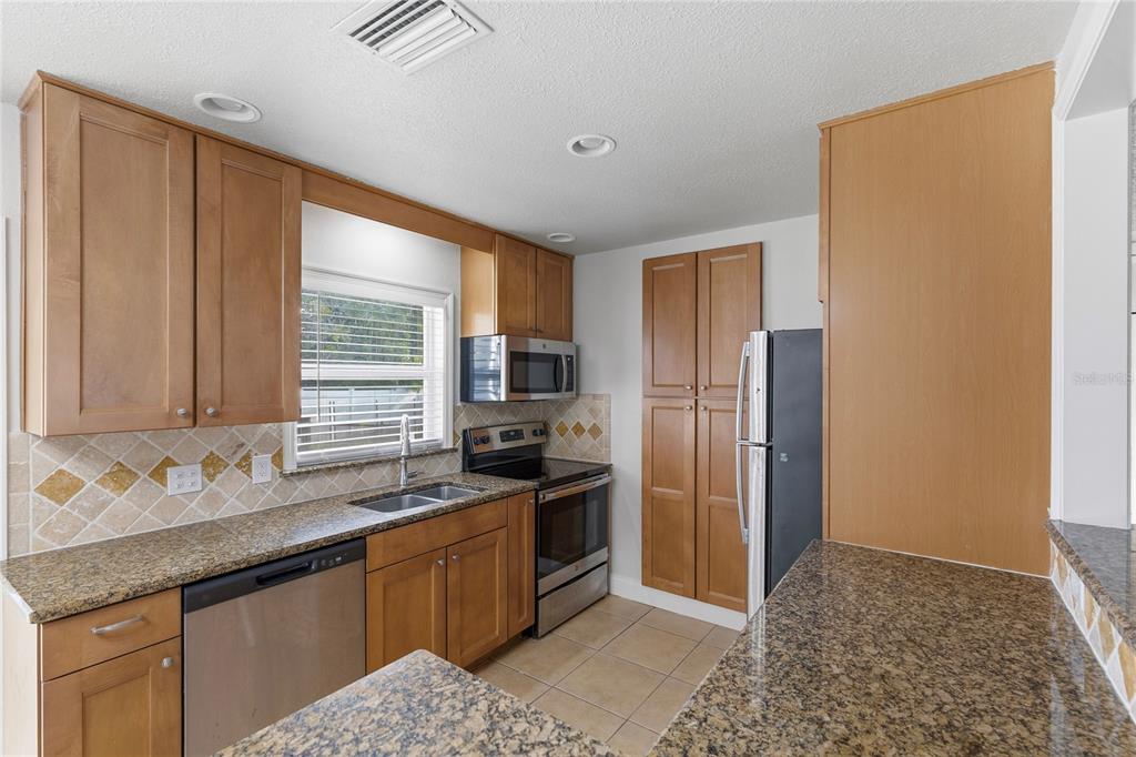 A kitchen features wood cabinets, granite countertops, stainless steel appliances, and a tiled backsplash — 2415 15TH STREET W, PALMETTO, FL
