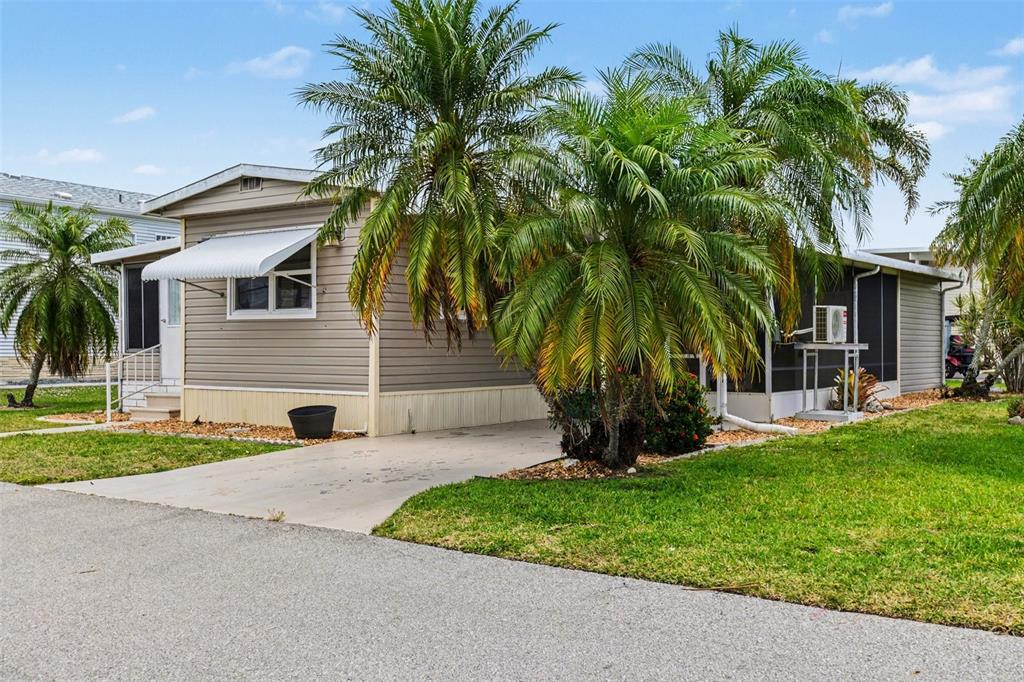 A single-story manufactured home with beige siding, a concrete driveway, and several palm trees — 20 HOLLAND DRIVE, PUNTA GORDA, FL