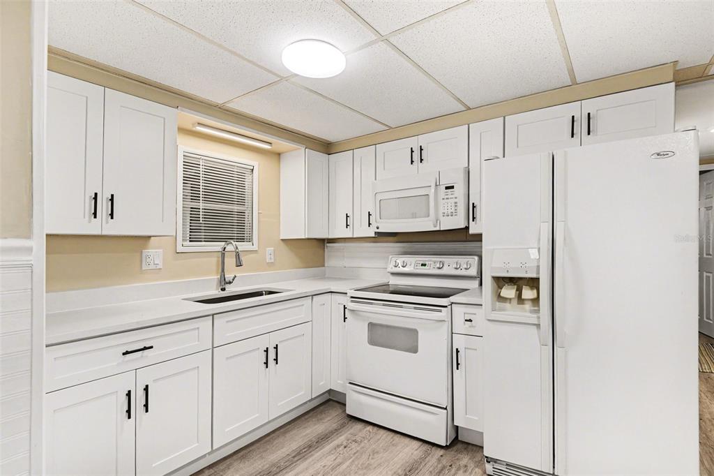 A kitchen featuring white cabinets, white appliances, a stainless steel sink, and light wood flooring — 20 HOLLAND DRIVE, PUNTA GORDA, FL
