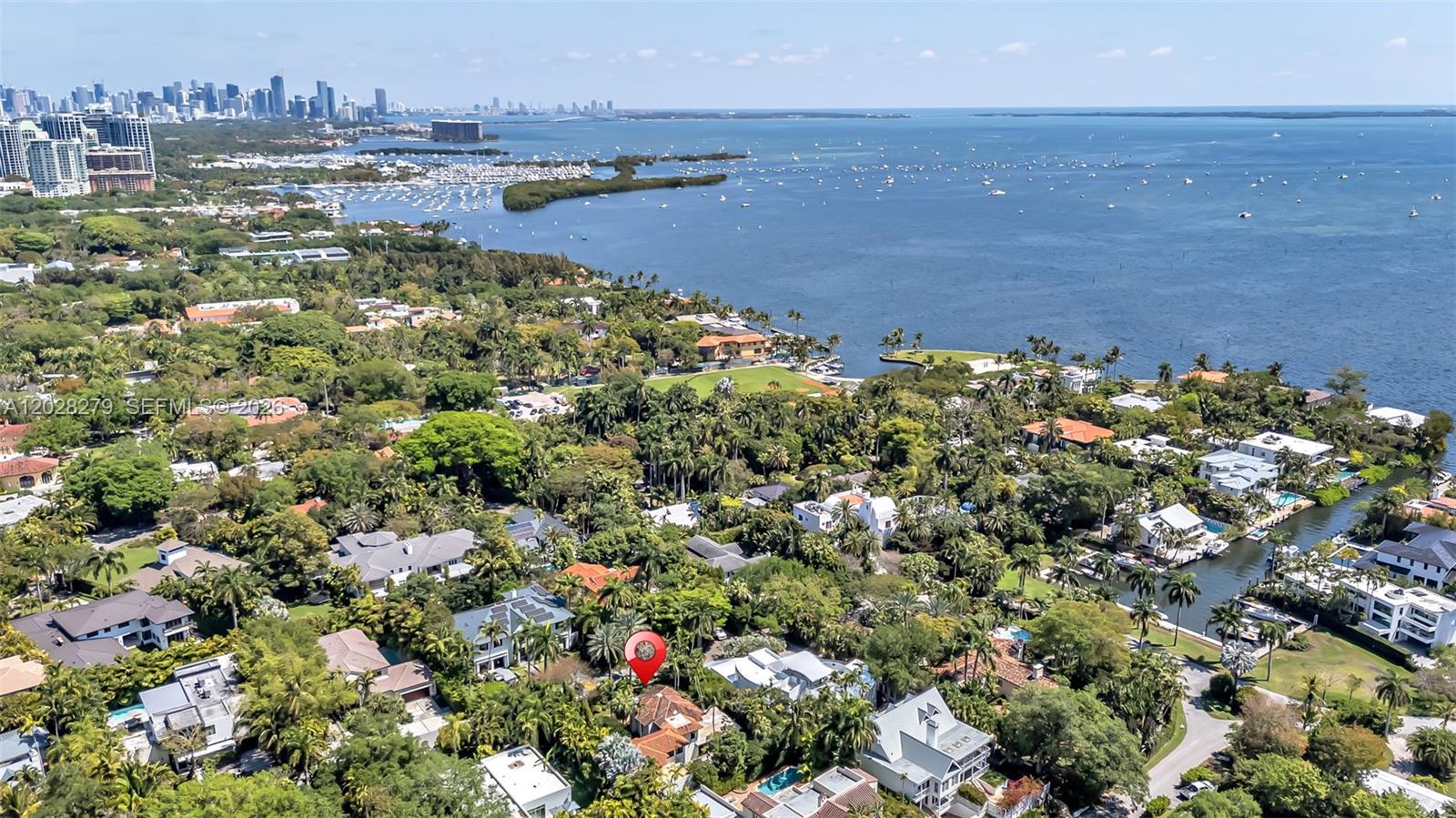 An aerial view shows a residential neighborhood with lush trees, houses, and a waterfront — 3462 N Moorings Way, Miami FL 33133, MIAMI, FL