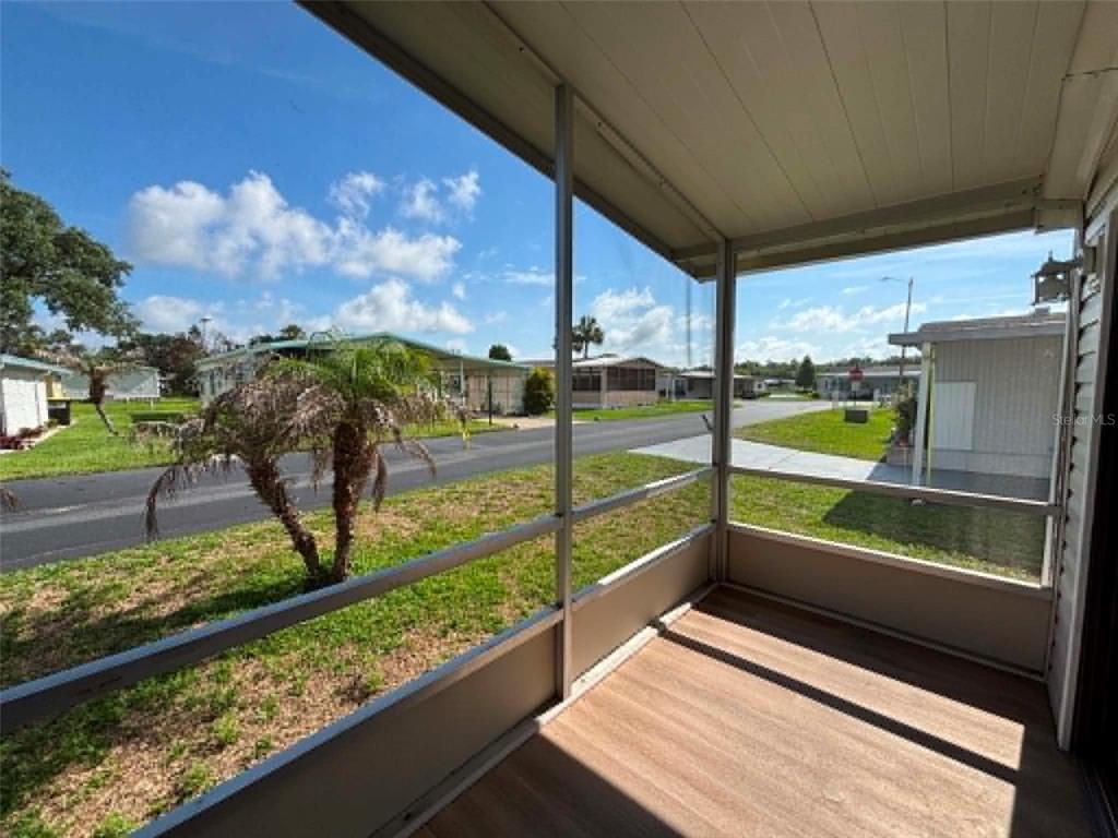 A screened-in porch with wood-look flooring overlooks a residential street and neighboring mobile homes — 1901 US HIGHWAY 17 92, LAKE ALFRED, FL