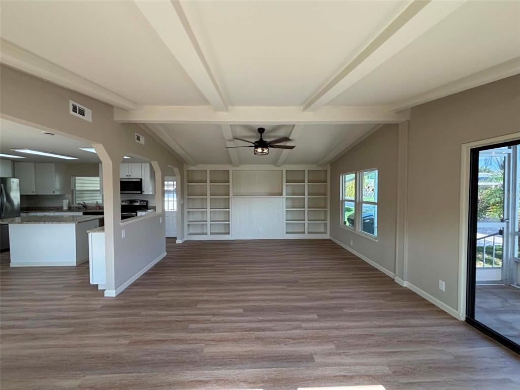 A spacious living room features wood-look flooring, a beamed ceiling, and built-in wall shelving — 1901 US HIGHWAY 17 92, LAKE ALFRED, FL