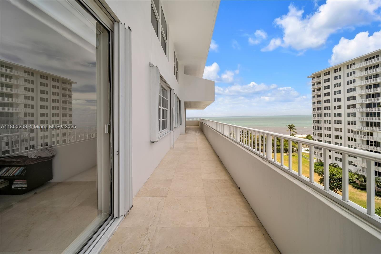 A long, tiled balcony overlooks the ocean with a white railing and adjacent high-rise buildings — 199 Ocean Lane Dr # 901, Key Biscayne FL 33149, KEY BISCAYNE, FL