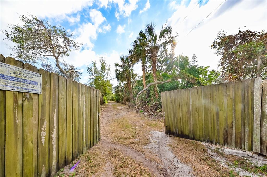 A dirt path leads through an open wooden gate into a wooded area with palm trees — 8839 RICHMOND STREET, GIBSONTON, FL